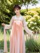 A woman in a pink and white hanbok standing in a garden.