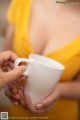 A woman in a yellow dress holding a white cup.
