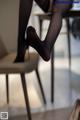 A woman in black stockings sitting on a chair.