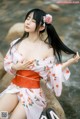 A woman in a pink kimono sitting on a rock by the water.