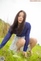 A woman in a blue shirt and white skirt crouching in the grass.