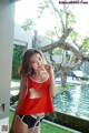 A woman in a red tank top and black shorts posing by a pool.