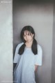 A woman in a white shirt leaning against a wall.