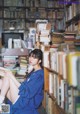 A woman sitting on the floor in front of a book shelf.