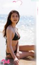 A woman in a black bikini sitting on the beach.