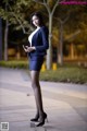 A woman in a business suit standing on a sidewalk looking at her phone.