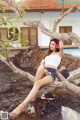 A woman sitting on a tree branch by a pool.