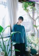 A woman standing in front of a window next to a plant.